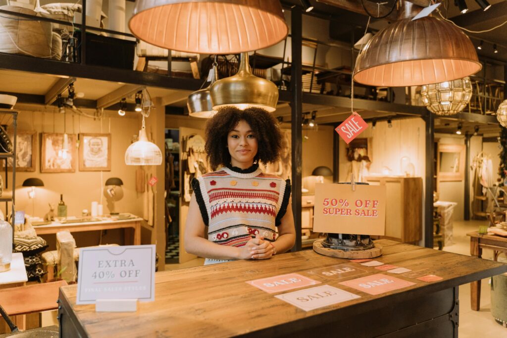 A cheerful saleswoman in a boutique during a super sale event with vibrant signage.